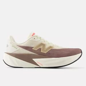 A New Balance FuelCell Rebel v4 running shoe, seen from a side view against a plain white background. The shoe features an off-white or light cream upper with a textured, breathable mesh. A large, stylized 'N' logo in a light brown or tan color is visible on the side, partially obscured by a darker, muted plum or reddish-brown material that extends across the midfoot. The sole is thick and chunky, primarily off-white with some darker brown accents and a black outsole. Small orange accents are visible on the tongue and near the sole, with 'FUELCELL' text printed on the midsole.