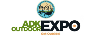 Logo for the ADK Outdoor Expo. At the top is a circular seal for the Adirondack Mountain Club - Genesee Valley Chapter, featuring silhouettes of flying ducks and cattails against a yellow and blue sky, with the motto "Working for Wilderness" at the bottom. Below the seal, the main text reads "ADK OUTDOOR EXPO" in a bold font, with "ADK OUTDOOR" in green and "EXPO" in large black letters with an orange target-like center in the letter 'O'. At the very bottom, the tagline "Get Outside!" is written in orange script.