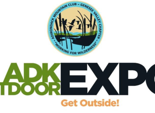 Logo for the ADK Outdoor Expo. At the top is a circular seal for the Adirondack Mountain Club - Genesee Valley Chapter, featuring silhouettes of flying ducks and cattails against a yellow and blue sky, with the motto "Working for Wilderness" at the bottom. Below the seal, the main text reads "ADK OUTDOOR EXPO" in a bold font, with "ADK OUTDOOR" in green and "EXPO" in large black letters with an orange target-like center in the letter 'O'. At the very bottom, the tagline "Get Outside!" is written in orange script.