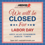 A sign for Medved Running & Walking Outfitters stating that the store will be closed for Labor Day. It notes that the store will reopen tomorrow from 10:00 AM to 7:00 PM and mentions that their online store is open 24/7 at medvedrunwalk.com. The sign features a patriotic theme with a red, white, and blue border decorated with stars.