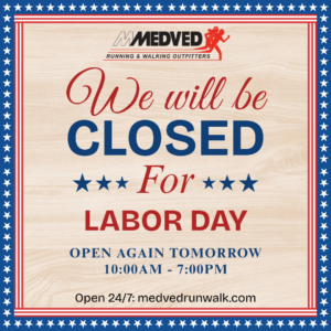 A sign for Medved Running & Walking Outfitters stating that the store will be closed for Labor Day. It notes that the store will reopen tomorrow from 10:00 AM to 7:00 PM and mentions that their online store is open 24/7 at medvedrunwalk.com. The sign features a patriotic theme with a red, white, and blue border decorated with stars.