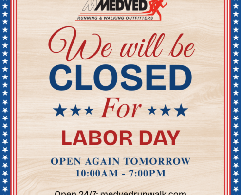 A sign for Medved Running & Walking Outfitters stating that the store will be closed for Labor Day. It notes that the store will reopen tomorrow from 10:00 AM to 7:00 PM and mentions that their online store is open 24/7 at medvedrunwalk.com. The sign features a patriotic theme with a red, white, and blue border decorated with stars.